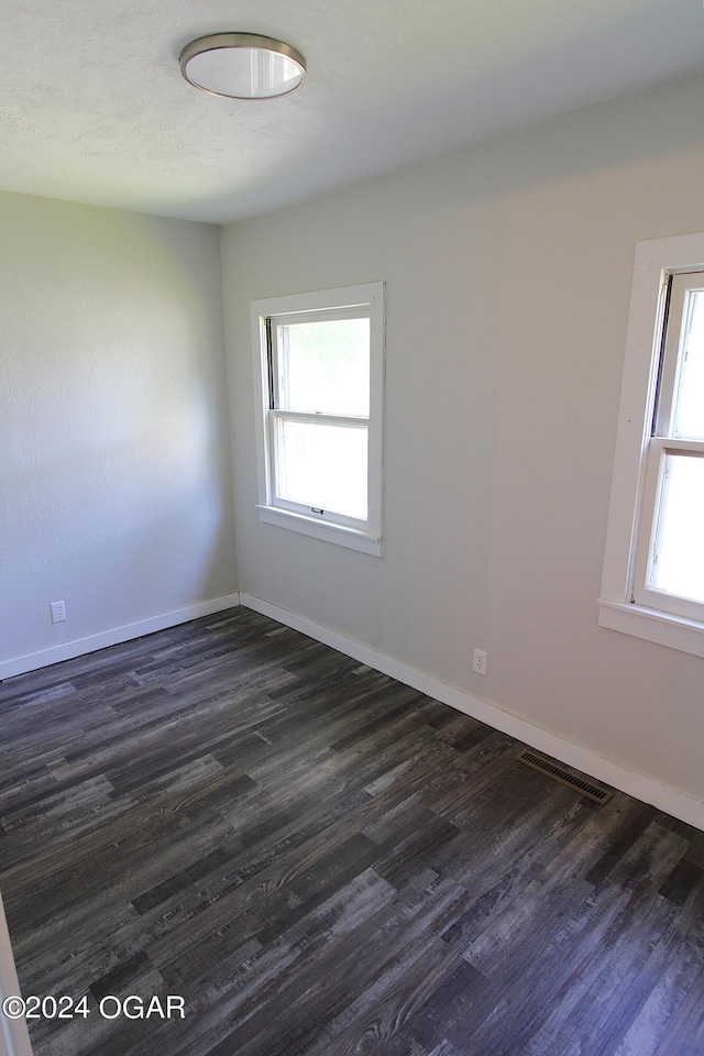 empty room with dark wood-style floors, visible vents, and baseboards