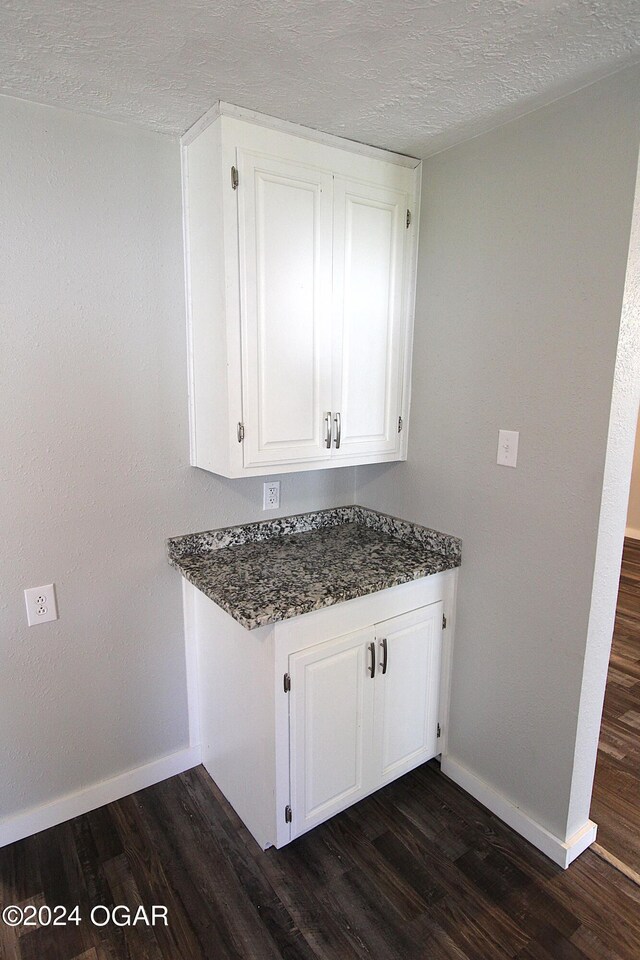 kitchen featuring a textured ceiling, dark wood-type flooring, white cabinetry, and dark stone countertops