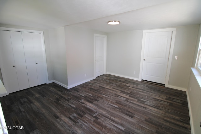 unfurnished bedroom with dark wood-style flooring, a closet, and baseboards