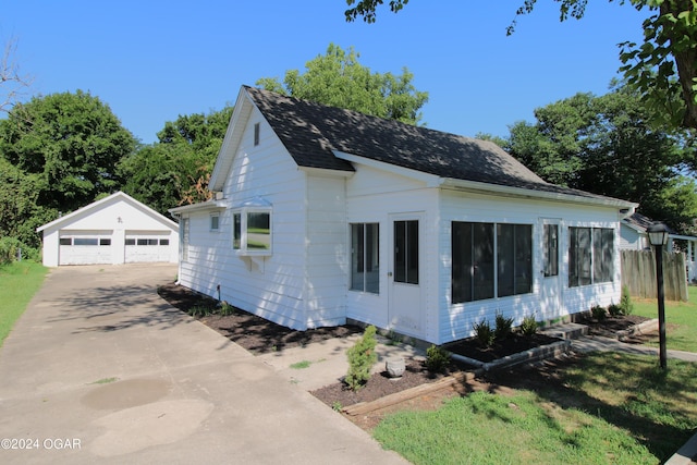 view of property exterior featuring roof with shingles, a detached garage, and an outdoor structure