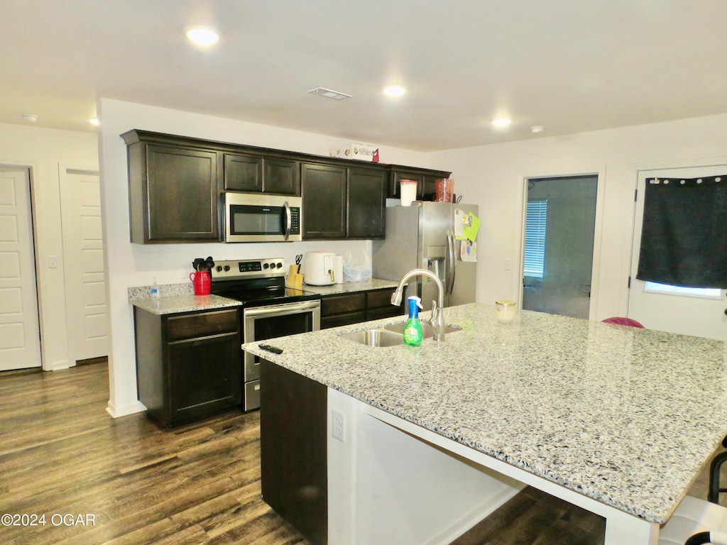 kitchen with stainless steel appliances, a kitchen breakfast bar, light stone counters, sink, and dark wood-type flooring