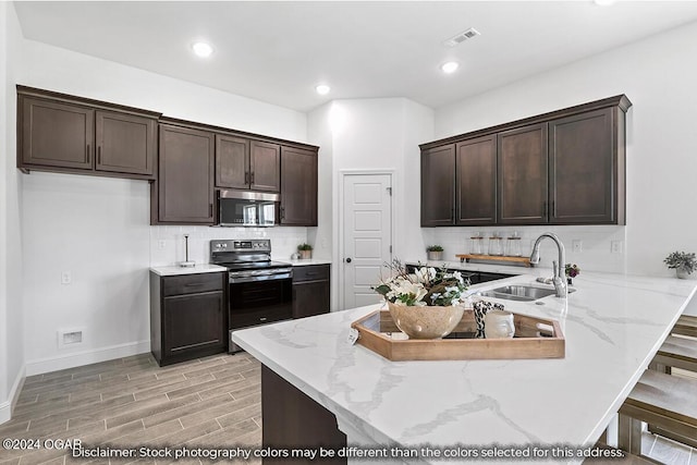 kitchen with sink, black / electric stove, light stone counters, tasteful backsplash, and kitchen peninsula