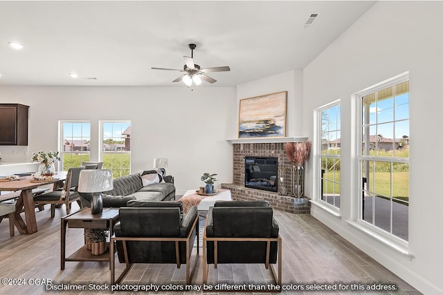 living room with light wood-type flooring, ceiling fan, and a brick fireplace