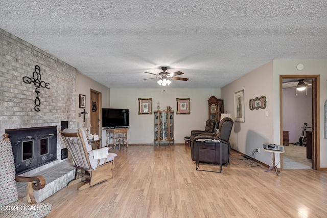 living room featuring a textured ceiling, a brick fireplace, ceiling fan, and light hardwood / wood-style floors