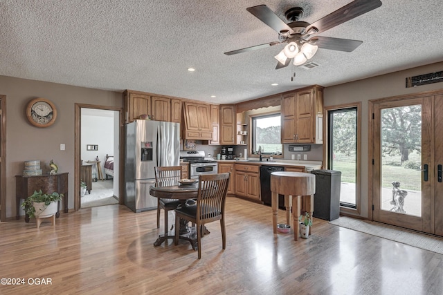 kitchen with a textured ceiling, sink, ceiling fan, appliances with stainless steel finishes, and light hardwood / wood-style floors