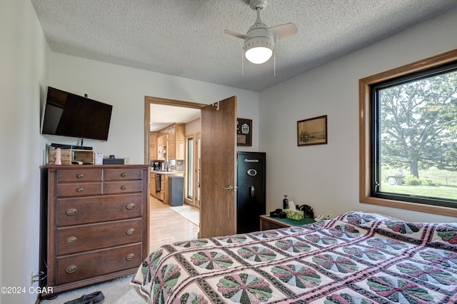 bedroom with light wood-type flooring, a textured ceiling, ensuite bathroom, and ceiling fan