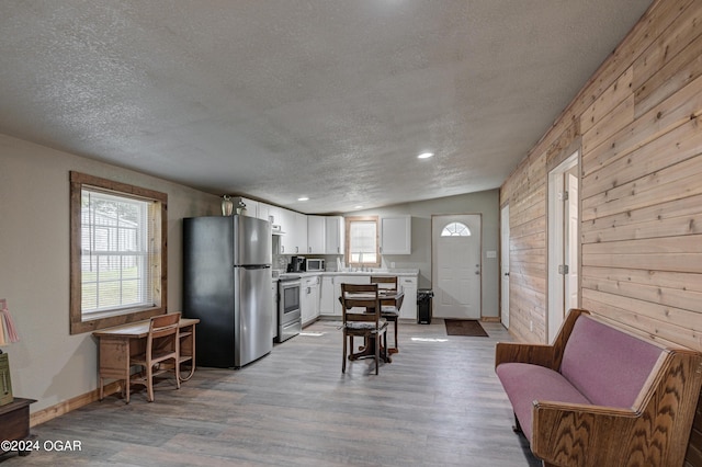 living room featuring light wood-type flooring, lofted ceiling, wooden walls, and a textured ceiling