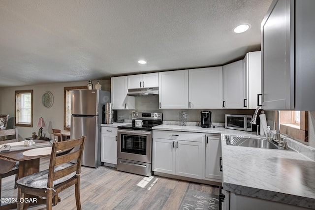 kitchen featuring stainless steel appliances, light hardwood / wood-style floors, white cabinetry, sink, and a textured ceiling