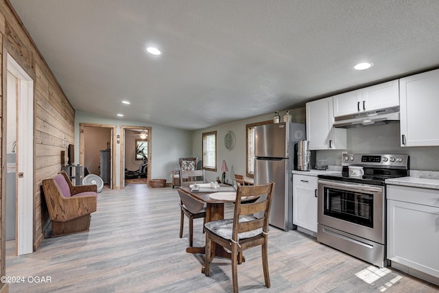 kitchen with light wood-type flooring, stainless steel appliances, a textured ceiling, and wooden walls