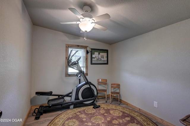 exercise room featuring lofted ceiling, ceiling fan, light hardwood / wood-style floors, and a textured ceiling