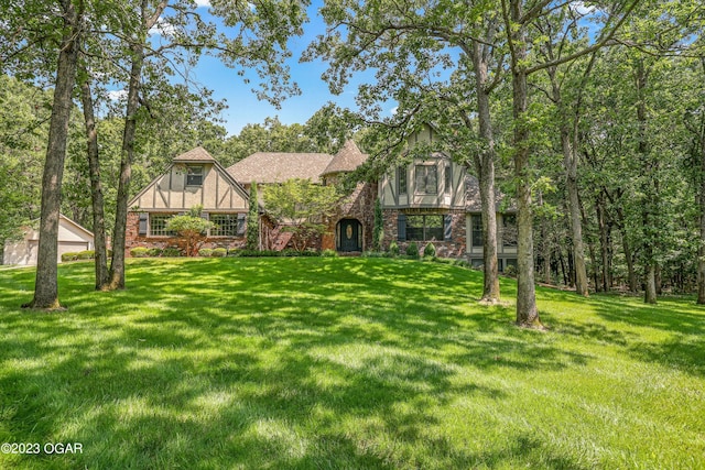 tudor house with brick siding, a front yard, and stucco siding