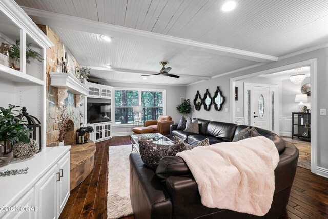 living room with ceiling fan, dark wood-type flooring, a fireplace, beamed ceiling, and crown molding