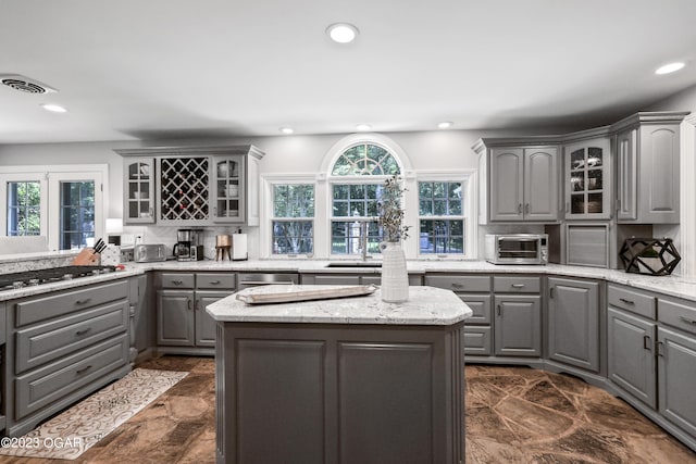 kitchen with stainless steel appliances, dark tile patterned floors, light stone counters, gray cabinetry, and a center island