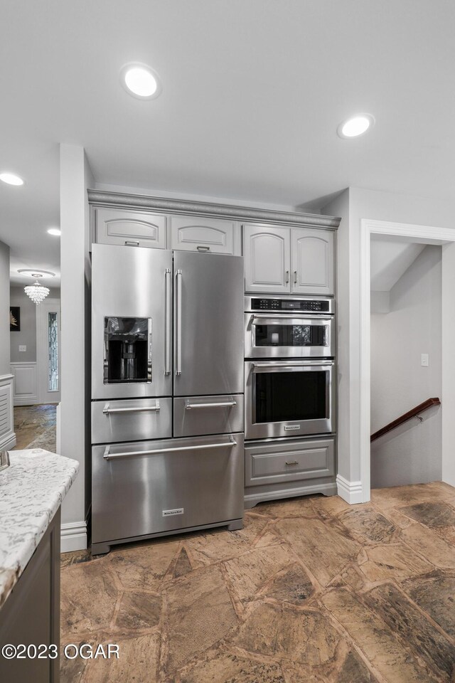 kitchen featuring gray cabinetry, stainless steel appliances, dark tile patterned flooring, and light stone counters