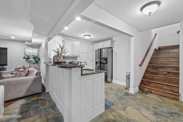 kitchen with dark stone counters, tile patterned flooring, white cabinetry, stainless steel fridge, and kitchen peninsula