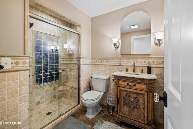 full bathroom with toilet, a wainscoted wall, vanity, tile walls, and a stall shower