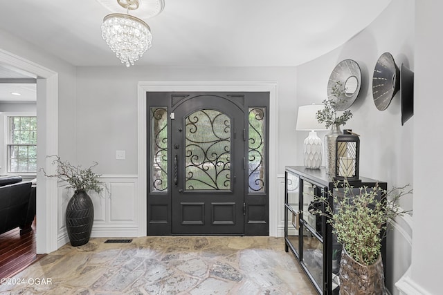 entryway with a chandelier, a wainscoted wall, a decorative wall, and visible vents