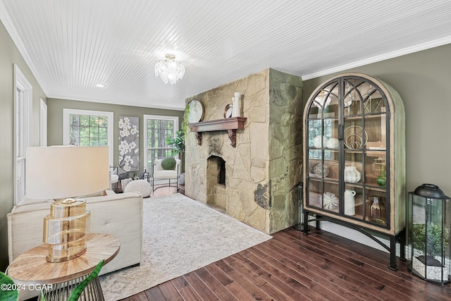 living room with a stone fireplace, wood-type flooring, ornamental molding, and a chandelier