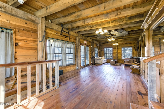 unfurnished living room featuring a notable chandelier, beam ceiling, wood ceiling, wood walls, and hardwood / wood-style floors