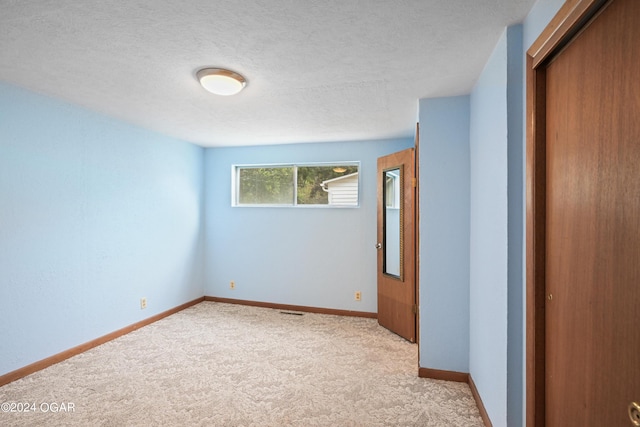 spare room featuring light colored carpet and a textured ceiling