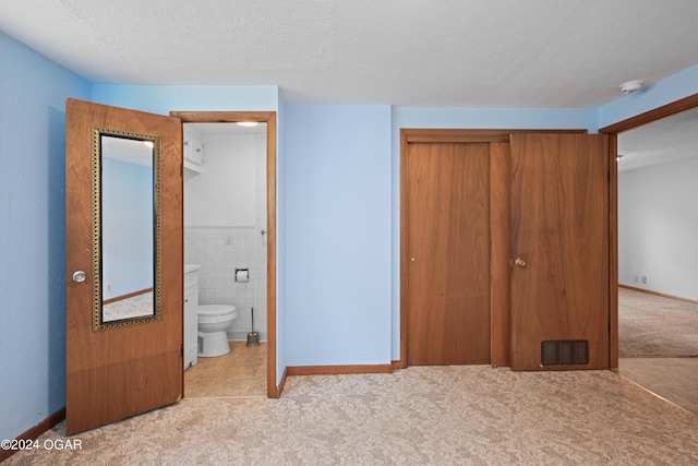 unfurnished bedroom featuring a textured ceiling, connected bathroom, a closet, and light carpet