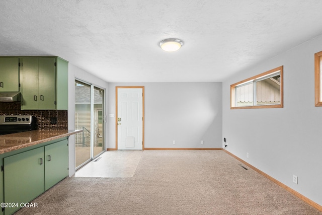 kitchen featuring green cabinets, light carpet, stainless steel range with electric stovetop, tasteful backsplash, and a textured ceiling