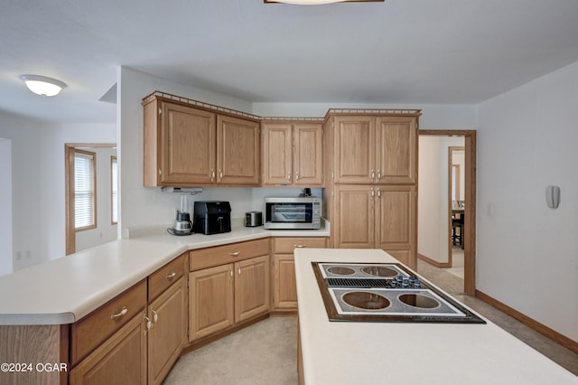 kitchen featuring baseboards, stainless steel microwave, a peninsula, black electric cooktop, and light countertops