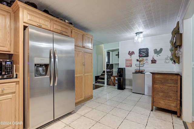 kitchen featuring wood walls, appliances with stainless steel finishes, light tile patterned floors, and light brown cabinets