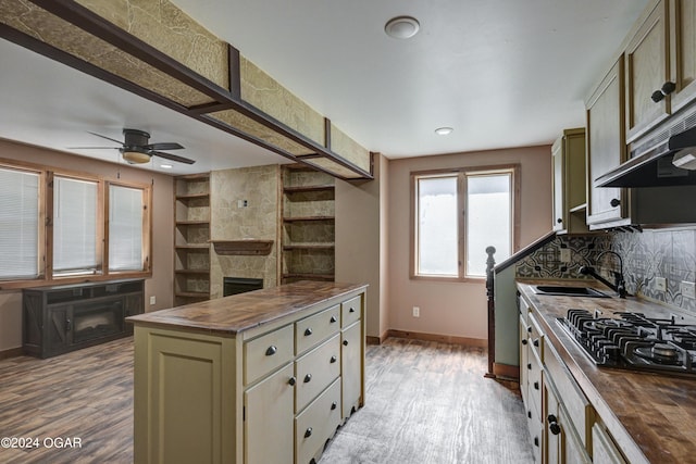 kitchen with a stone fireplace, hardwood / wood-style floors, sink, ceiling fan, and butcher block counters