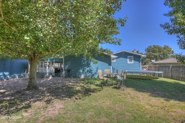 rear view of property with a trampoline and a lawn