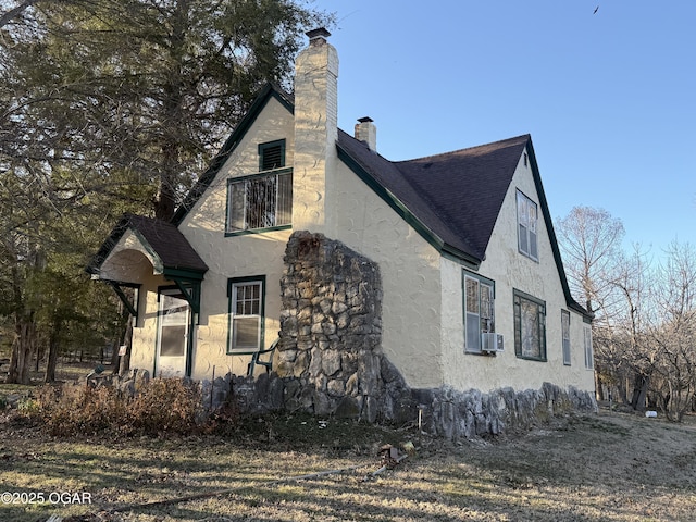 view of property exterior featuring roof with shingles, a chimney, cooling unit, and stucco siding