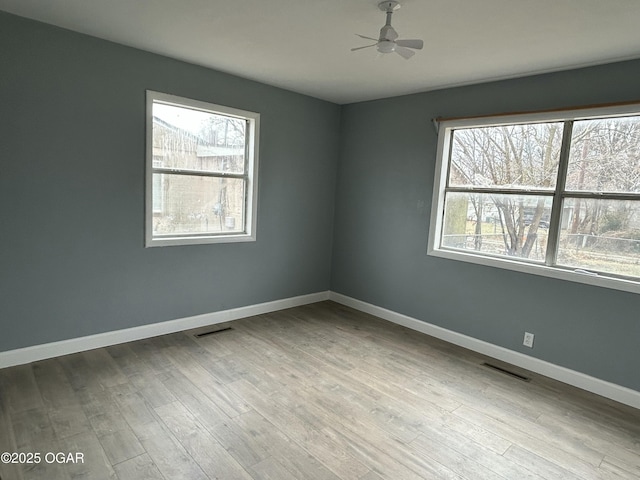 unfurnished room with a ceiling fan, visible vents, baseboards, and wood finished floors