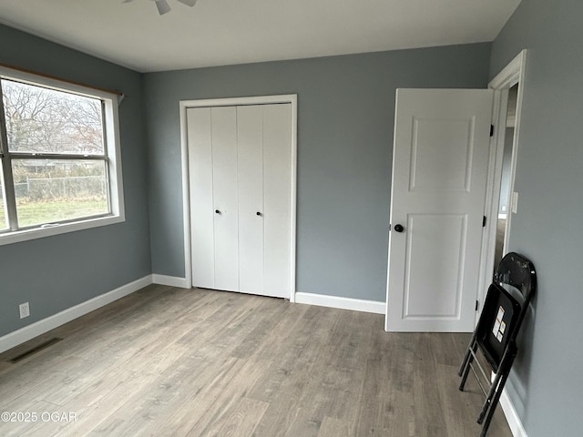 unfurnished bedroom with a closet, wood finished floors, visible vents, and baseboards