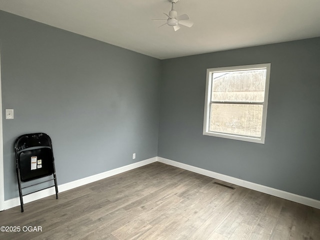 empty room featuring a ceiling fan, baseboards, visible vents, and wood finished floors