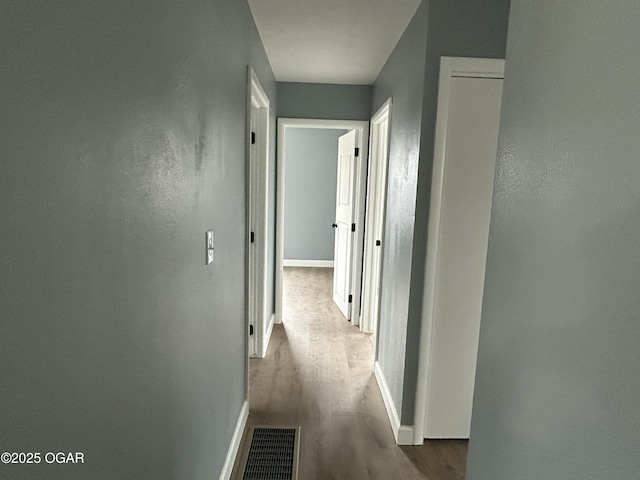 hallway with baseboards, visible vents, and wood finished floors