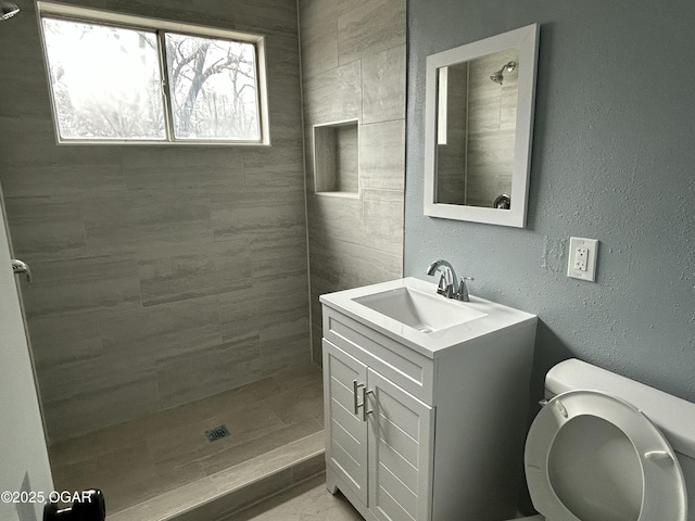 full bathroom with toilet, a textured wall, a shower stall, and vanity