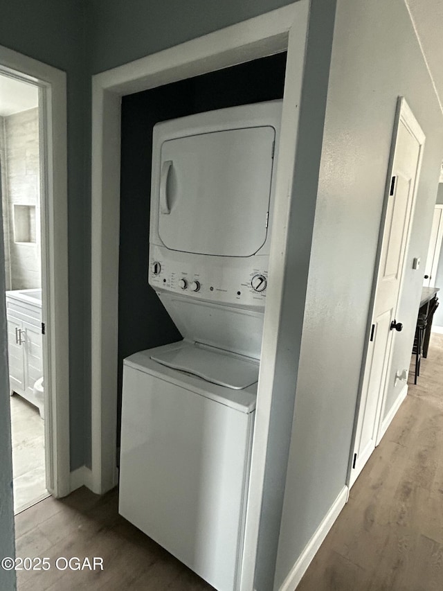 laundry room with baseboards, laundry area, wood finished floors, and stacked washer / drying machine