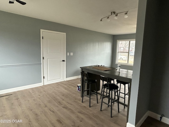 dining area featuring rail lighting, visible vents, ceiling fan, wood finished floors, and baseboards