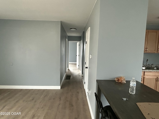 hallway with wood finished floors, a sink, visible vents, and baseboards