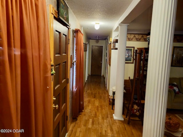 corridor with a textured ceiling, decorative columns, and light hardwood / wood-style floors