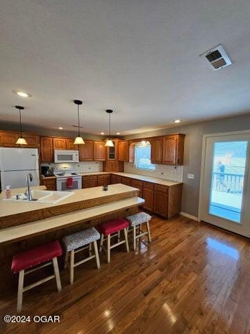 kitchen with backsplash, white appliances, dark hardwood / wood-style flooring, sink, and a breakfast bar area