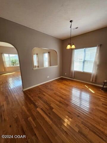 spare room with wood-type flooring and an inviting chandelier