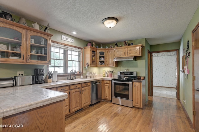 9825 County Rd 215, Webb City, MO 64870 - kitchen featuring stainless steel appliances, a sink, light wood-style flooring, a textured ceiling, and glass insert cabinets