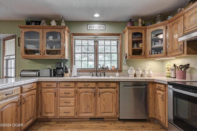 9825 County Rd 215, Webb City, MO 64870 - kitchen with appliances with stainless steel finishes, a sink, a textured ceiling, light wood-style floors, and glass insert cabinets