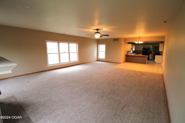 unfurnished living room with ceiling fan with notable chandelier and light colored carpet