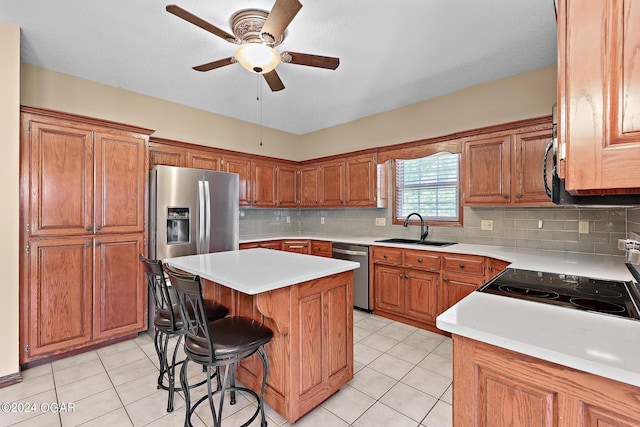 kitchen with a breakfast bar, a center island, sink, stainless steel appliances, and ceiling fan