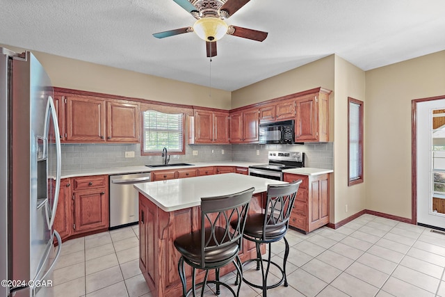 kitchen with sink, a kitchen bar, a kitchen island, appliances with stainless steel finishes, and ceiling fan