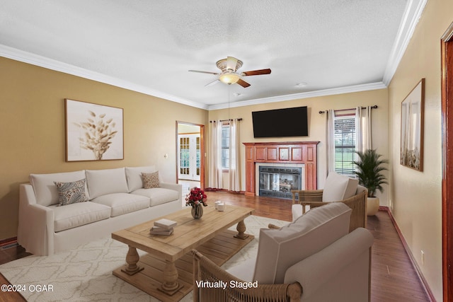 living room with a textured ceiling, wood-type flooring, ornamental molding, and ceiling fan