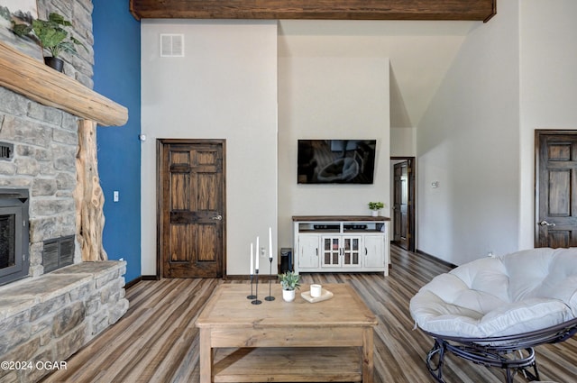 living room with a high ceiling, a stone fireplace, beam ceiling, and hardwood / wood-style floors