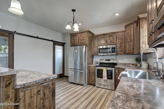 kitchen featuring sink, a notable chandelier, a barn door, appliances with stainless steel finishes, and decorative light fixtures